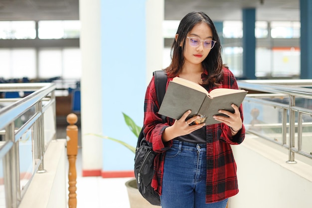 Vrouwelijke student die een boek leest terwijl hij in de bibliotheek staat