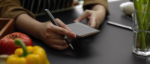 Vrouwelijke student die informatie over lege het schermsmartphone kijken in het koken klasse