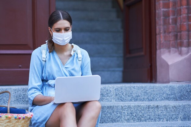 Vrouwelijke student die op de campus rondhangt met een beschermend masker vanwege de pandemie van het coronavirus