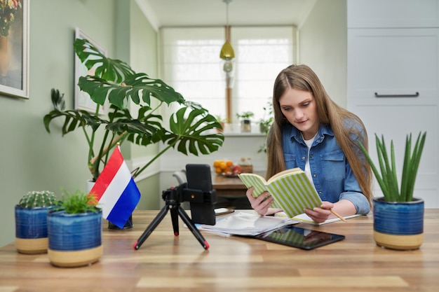 Vrouwelijke student die thuis zit en online studeert en naar de webcam van een smartphone kijkt
