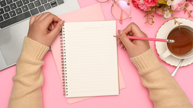 Vrouwelijke student doet huiswerk en schrijft essay op haar schoolnotitieboekje in haar roze bureau