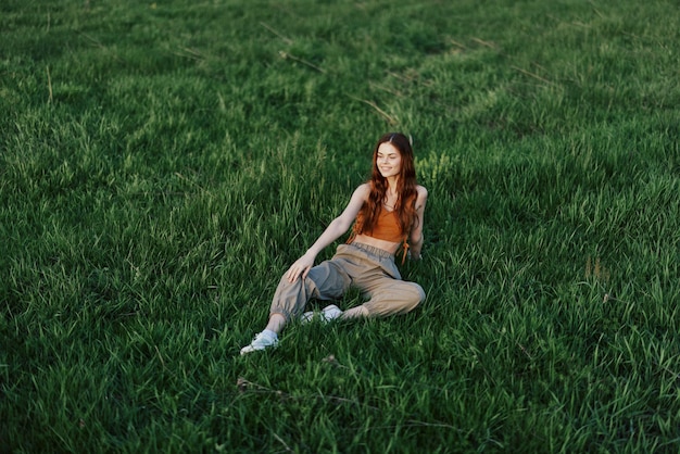 Vrouwelijke student freelancer zit op het gras in het park en kijkt naar de zonsondergang het concept van harmonie met de wereld en de natuur