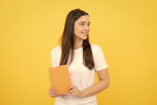 Vrouwelijke student houdt boeken op een gele achtergrond in een studio in handen Engels taal school onderwijsconcept