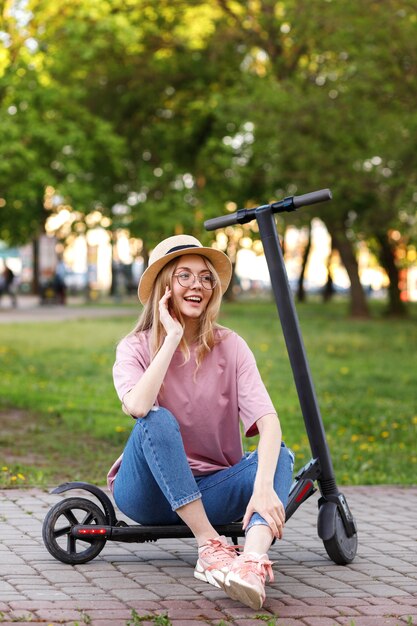 Vrouwelijke student in een hoed met een elektronische scooter op een wandeling in de zomer