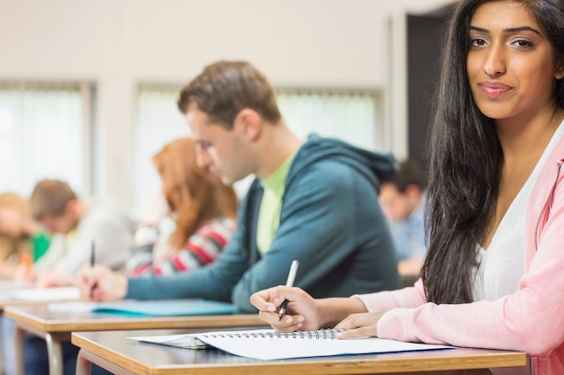 Vrouwelijke student met anderen schrijven van notities in de klas