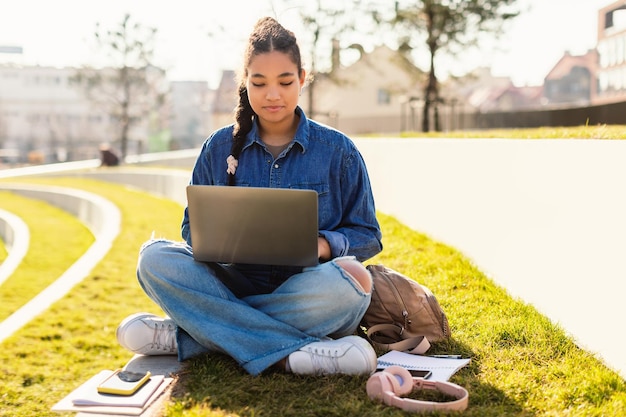 Foto vrouwelijke student van gemengd ras die met laptop in het park zit en online leert met educatieve virtuele