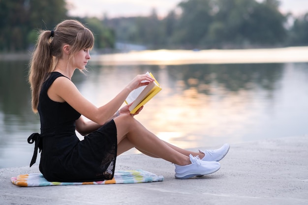 Vrouwelijke student zit in het zomerpark en leest leerboek buitenshuis. onderwijs en sudy concept.