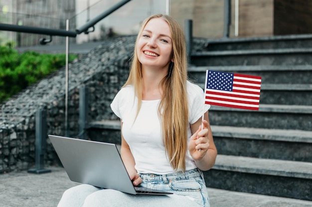 Vrouwelijke student zittend op de trap met laptop en met een kleine Amerikaanse vlag