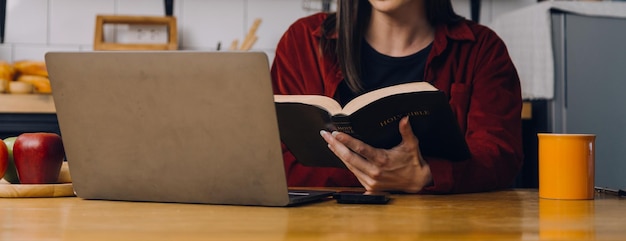 Vrouwelijke studenten noteren uit de boeken van de Aziatische meisjesbibliotheek die op de bank zit met een laptop en tablet om online informatie in de woonkamer te doorzoeken