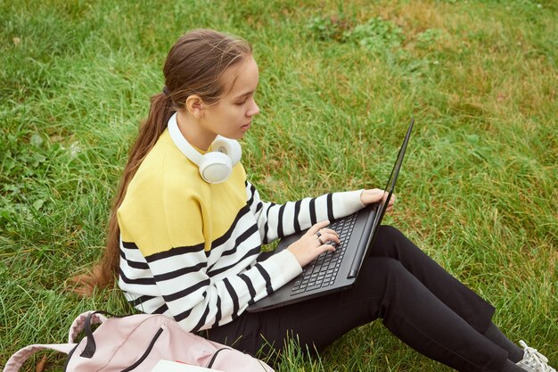 Foto vrouwelijke studentenmeisje gebruikt een laptop terwijl ze op het gras van de campus zit