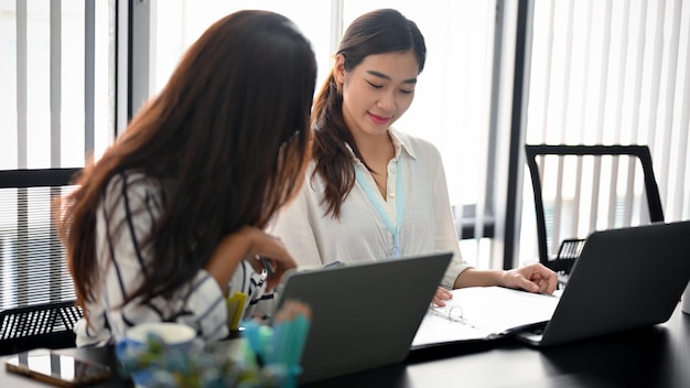 Vrouwelijke supervisor die het werk aan de rapportbestandsmap uitlegt aan haar collega zit aan het bureau. zakenvrouwen of vrouw werknemer concept.