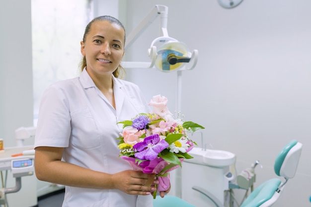 Vrouwelijke tandarts die, met een boeket van bloemen glimlacht