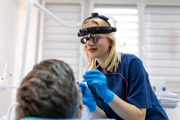 Vrouwelijke tandarts die tanden behandelt aan een patiënt van middelbare leeftijd als voorzitter bij tandheelkundige kliniek Tandheelkunde, gezonde tanden, geneeskunde en gezondheidszorgconcept