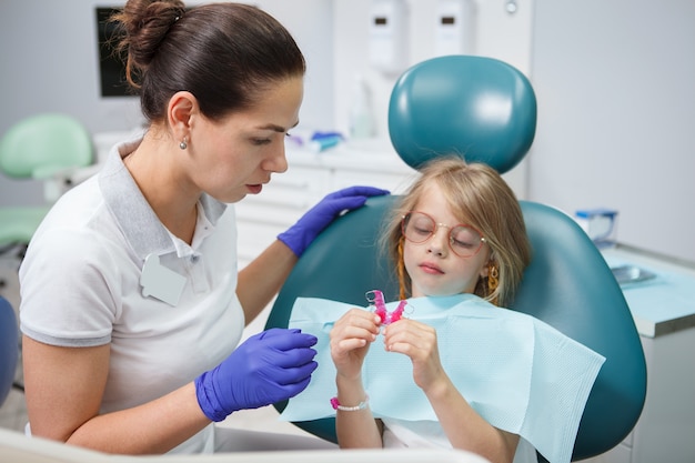 Vrouwelijke tandarts die verwijderbare tandplaat toont aan haar kleine patiënt