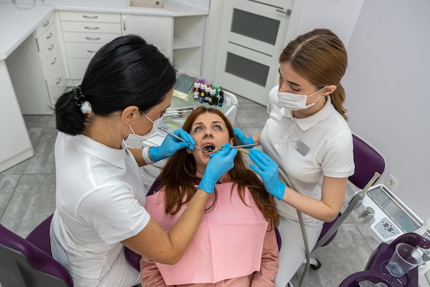 Vrouwelijke tandarts en een vrouwelijke assistent in een speciaal uniform behandelen de tanden van een vrouwelijke patiënt Een tandarts met een assistent aan het werk in een tandartspraktijk Concept van tandheelkunde en gezondheidszorg