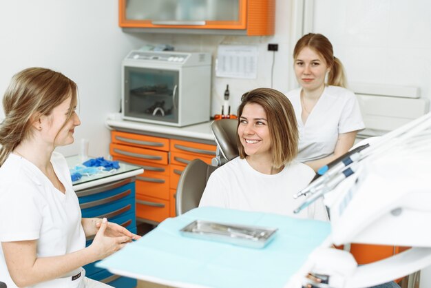 Vrouwelijke tandarts en haar assistent in tandartspraktijk praten met vrouwelijke patiënt
