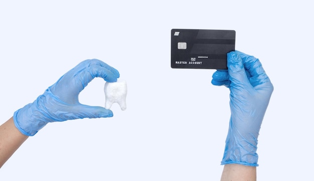 Vrouwelijke tandarts hand in blauwe handschoenen houdt tandarts Tand model en creditcard Lichte achtergrond Concept van kosten van tandheelkundige behandeling