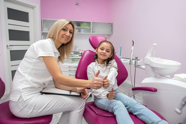 Vrouwelijke tandarts interviewt kleine meisjespatiënt in het kantoor van de tandheelkundige kliniek voor kinderen