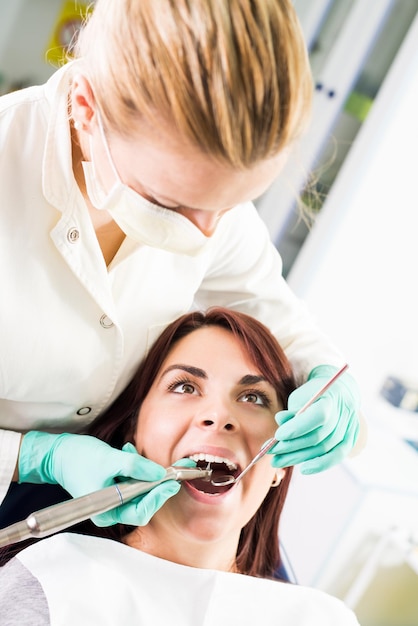 Vrouwelijke tandarts met tandheelkundige boor reparatie tand op de vrouwelijke patiënt op kantoor. Selectieve focus, focus op de patiënt.