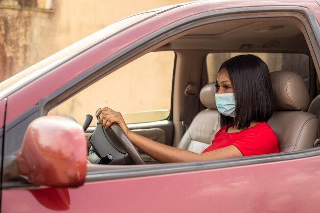 Vrouwelijke taxichauffeur met een rode tshite die het stuur vasthoudt met een neusmasker aan