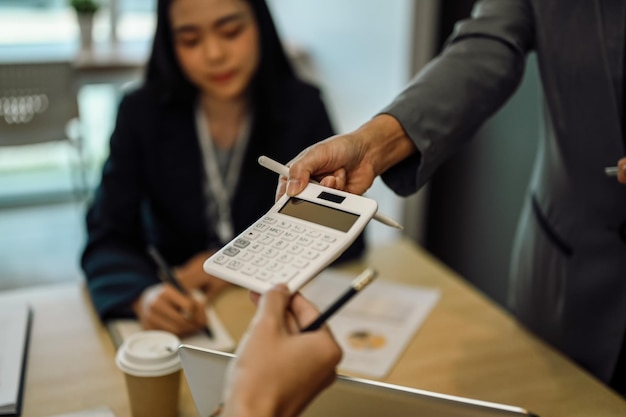 Vrouwelijke teamleider die financiën of berekeningen op een rekenmachine toont aan collega's in een vergadering