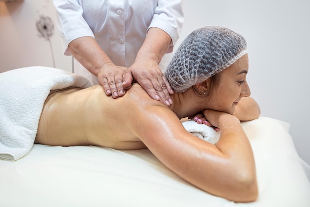 Vrouwelijke therapeut wrijft over de rug van een dame en geeft haar een ontspannende massage Close-up van de handen van de masseur die de rug masseren Lichaamsverzorging massage Spa concept
