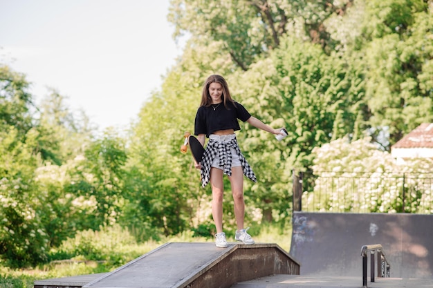 Vrouwelijke tiener met een skateboard die op de helling in het skatepark loopt