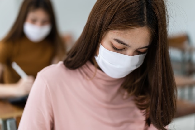 Vrouwelijke tienerstudenten dragen gezichtsmasker en houden afstand tijdens het studeren in de klas en op de universiteitscampus om covid-19-pandemie te voorkomen