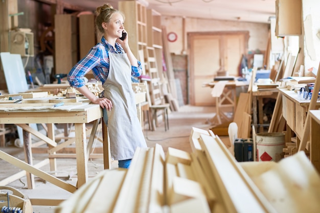 Vrouwelijke timmerman spreken door Smartphone in moderne werkplaats