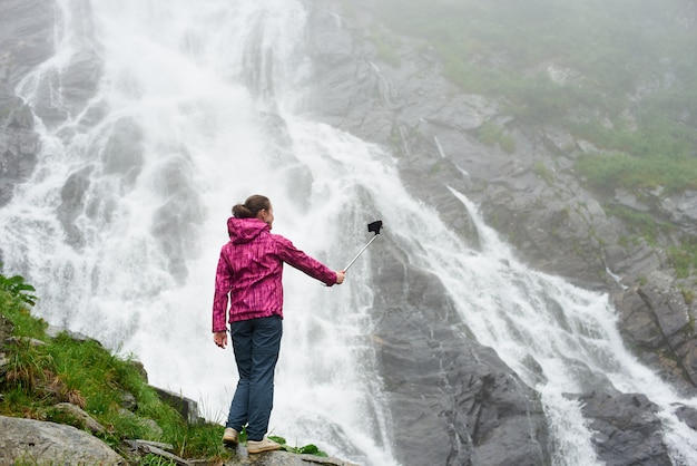 Vrouwelijke toerist die een selfie poseren in de buurt van prachtige rotsachtige waterval in de bergen