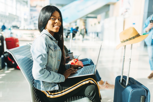 Vrouwelijke toerist die met laptop op vertrek in luchthaven wacht.