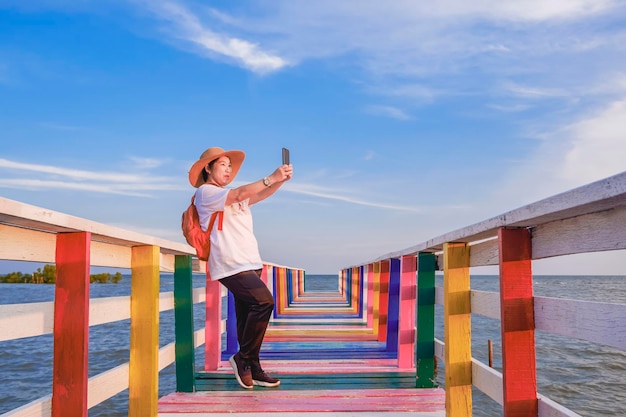 Vrouwelijke toerist die smartphone gebruikt om selfie te nemen op de houten regenboogbrug op zeegezichtspunt