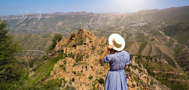 Vrouwelijke toerist hoog in de bergen van Dagestan bewondert het adembenemende panoramische uitzicht op de natuur en de oude verlaten stad Gamsutl. Kaukasus-gebergte, toeristische attractie, ruïnes, trektocht