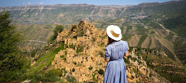 Vrouwelijke toerist hoog in de bergen van Dagestan bewondert het adembenemende panoramische uitzicht op de natuur en de oude verlaten stad Gamsutl. Kaukasus-gebergte, toeristische attractie, ruïnes, trektocht