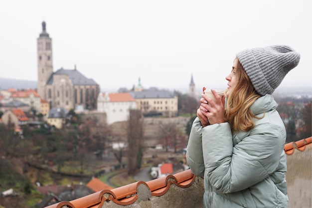 Vrouwelijke toerist tegen de achtergrond van de stad in de Tsjechische Republiek - Kutna Hora. Ze drinkt glühwein - herfstseizoen