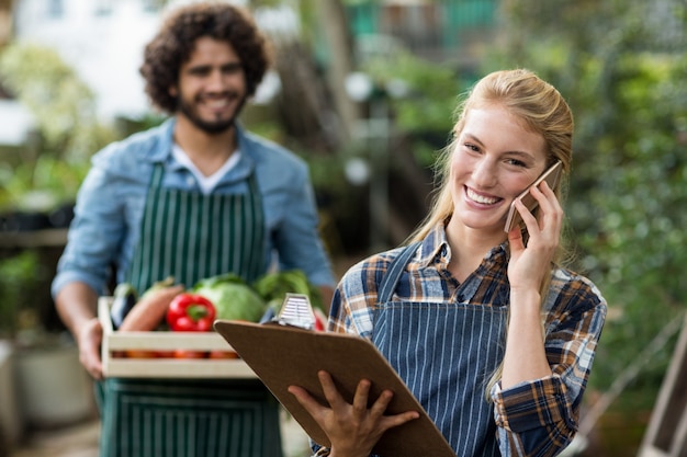 Vrouwelijke tuinman die op mobiele telefoon spreekt terwijl mens status