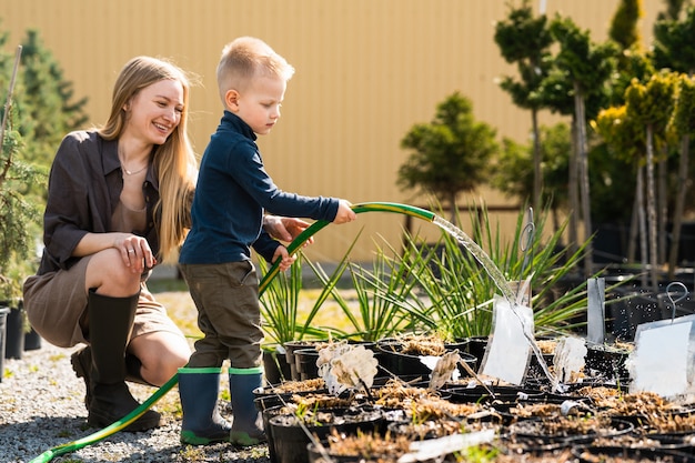 Vrouwelijke tuinman en haar zoon die de planten in potten water geven met een tuinslang