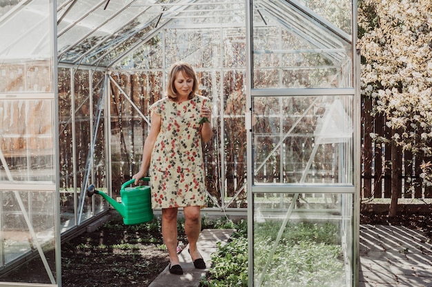 Vrouwelijke tuinman geeft planten in kas water. Ze houdt een plastic groene gieter vast.