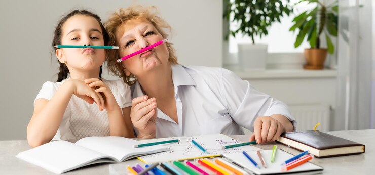 Vrouwelijke tutor of pleegoudermoeder die schattig Kaukasisch schoolkind helpt met huiswerk dat aan tafel zit. Diverse oppas en kind leren schrijven in notitieboekje thuis studeren.