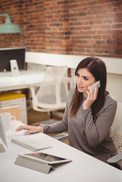 Vrouwelijke uitvoerend die op mobiele telefoon bij bureau spreekt