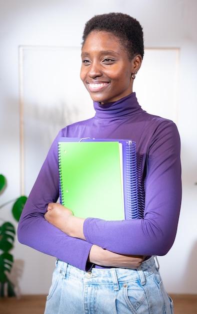 Vrouwelijke universiteitsstudent gelukkige lieve zwarte vrouwelijke student houdt boeken en notitieboeken in haar hand