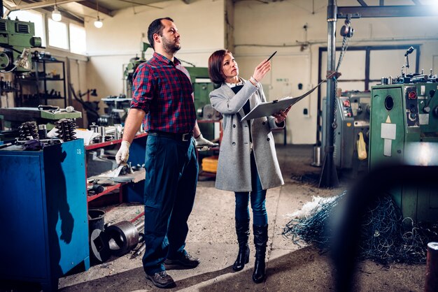 Foto vrouwelijke veiligheidsinspecteur die met machinist bij fabriek spreken