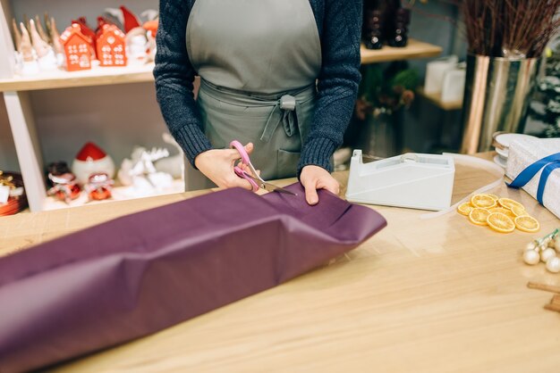 Vrouwelijke verkoper snijdt het inpakpapier met een schaar, decoratie van de geschenkdoos.