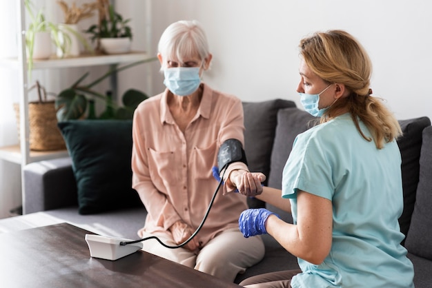 Vrouwelijke verpleegster met medisch masker met behulp van een bloeddrukmeter op oudere vrouw