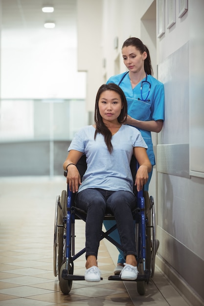 Vrouwelijke verpleegsters bijwonende patiënt op rolstoel in gang