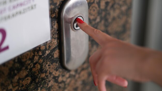 Vrouwelijke vinger met rode manicure op de close-up van de liftknop