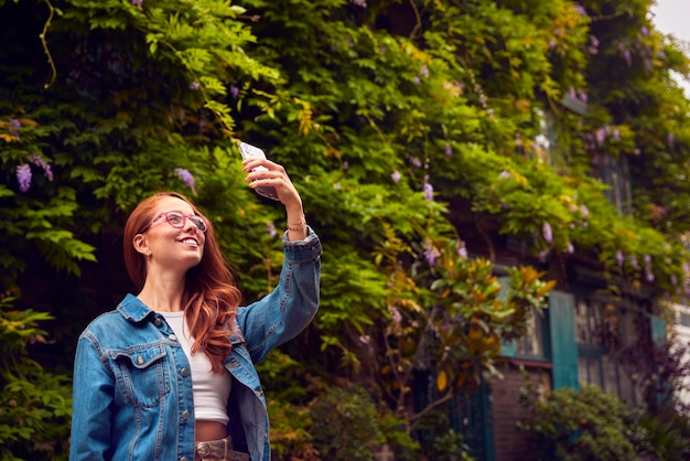 Vrouwelijke vlogger of sociale beïnvloeder in de stad die selfie op mobiele telefoon neemt om op sociale media te posten