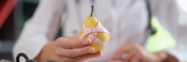 Vrouwelijke voedingsdeskundige toont perenfruit met meetlint en raadt aan om gezond te eten