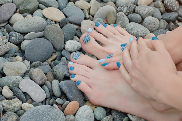 Vrouwelijke voeten en handen met een blauwe manicure op kiezels