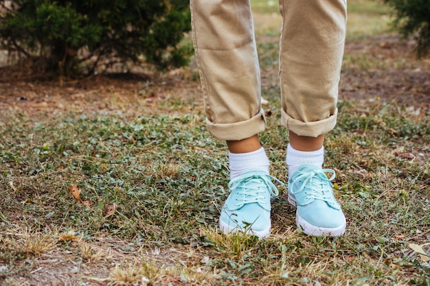 Vrouwelijke voeten in beige broek en turkooise tennisschoenen die zich op het gras dichtbij de bomen bevinden